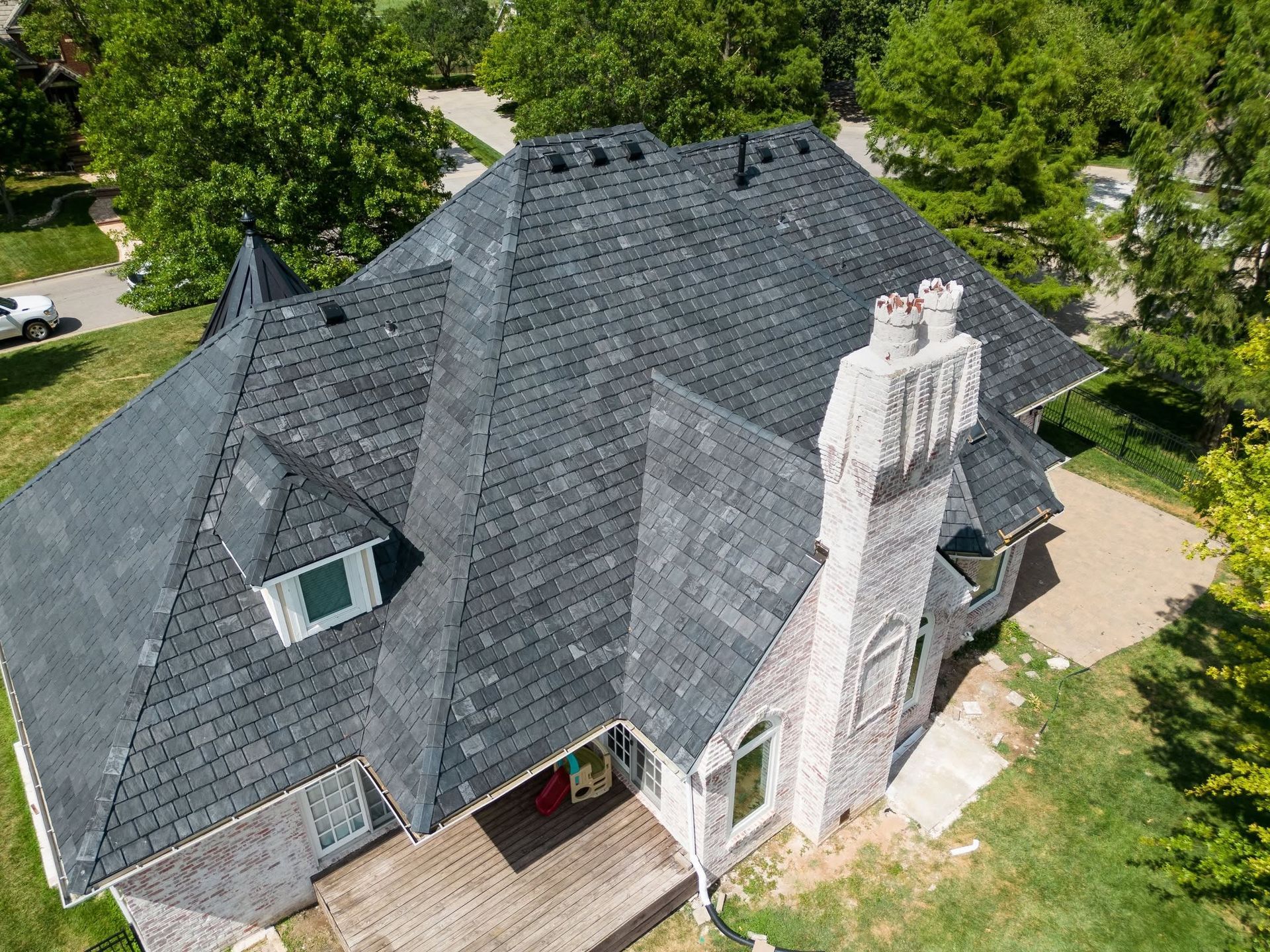 Aerial view of a gray-roofed house with a brick chimney and surrounding green trees.