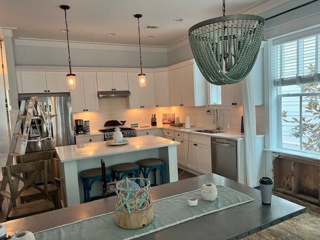 Bright white kitchen with island, pendant lights, large window, and green chandelier light fixture