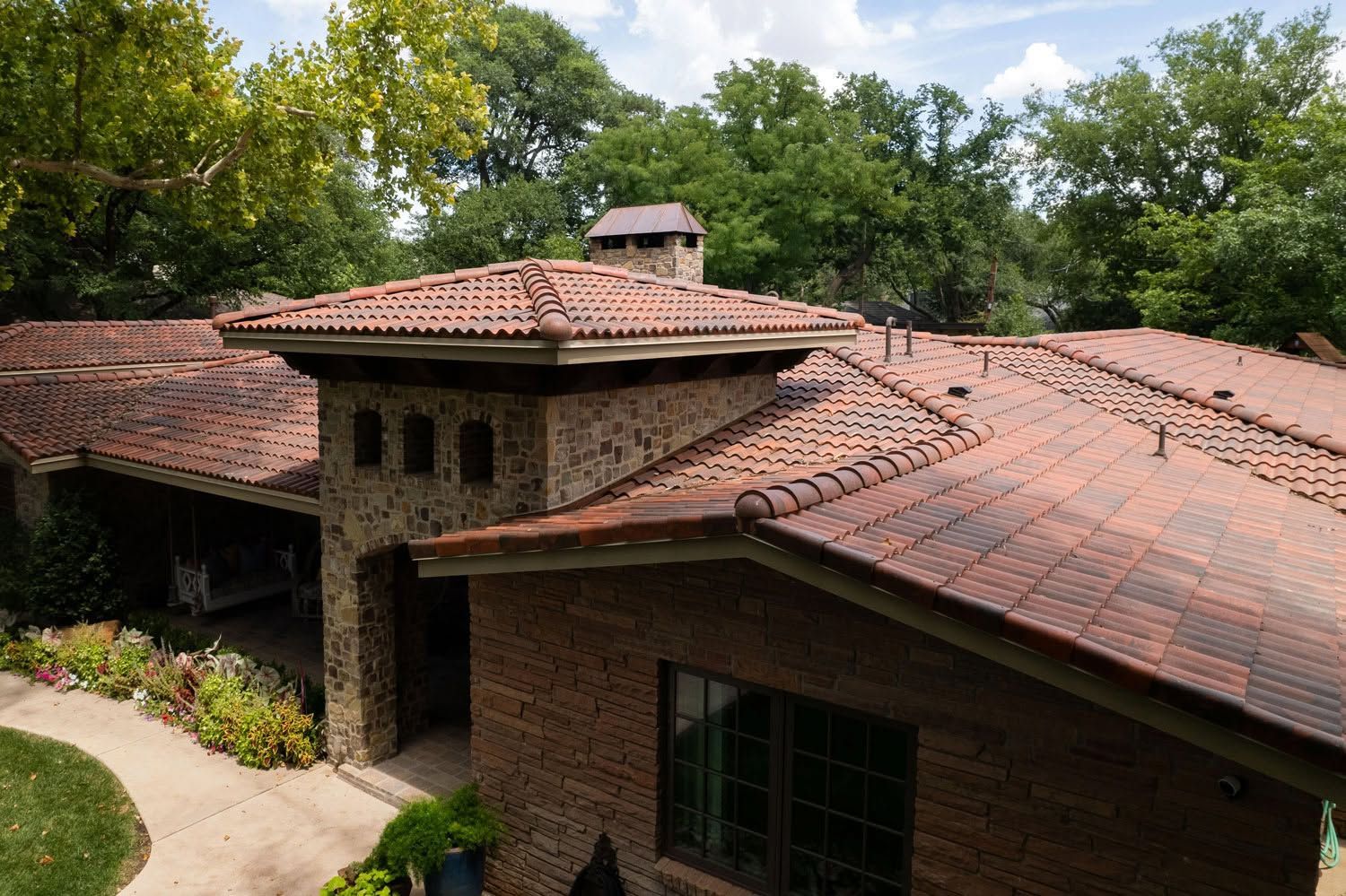 Brick house with red tiled roof and large windows, surrounded by trees and greenery