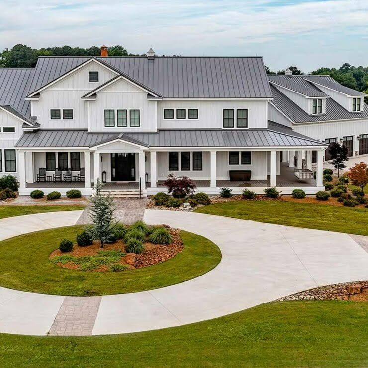 Large white house with gray metal roof, front porch, and circular driveway with landscaped lawn