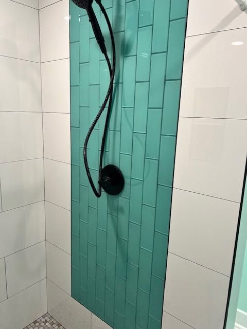 Shower with turquoise tile accent wall, black handheld shower hose, and white tiled sides