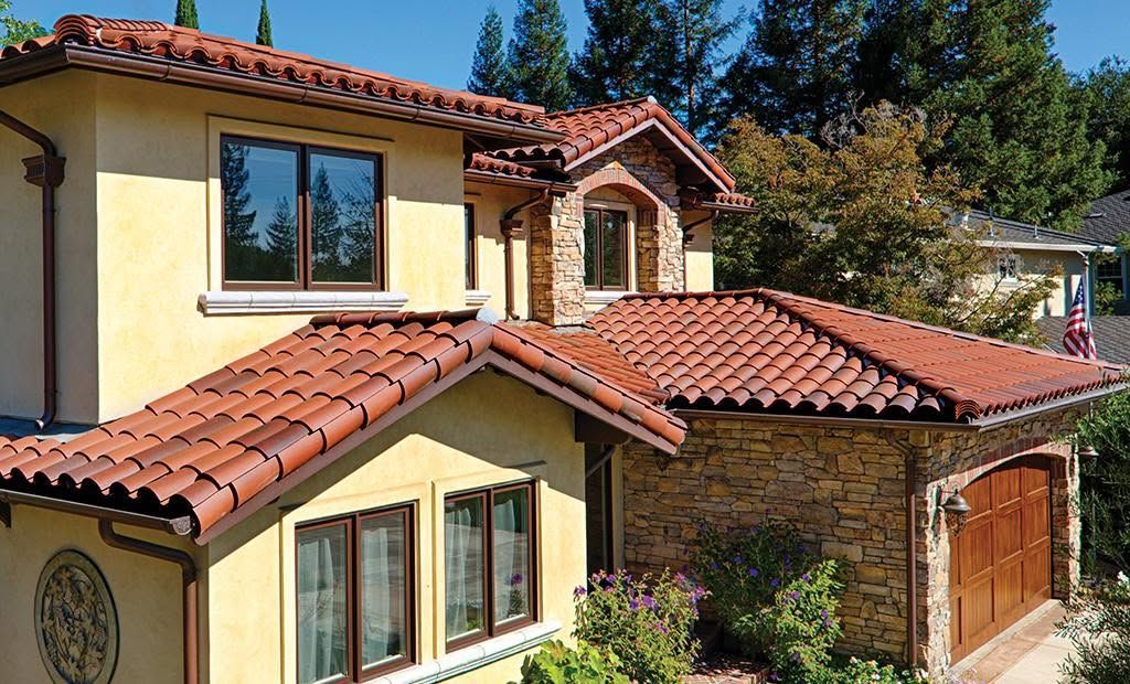 Two-story stucco house with red tile roofs and a wooden garage, surrounded by trees.