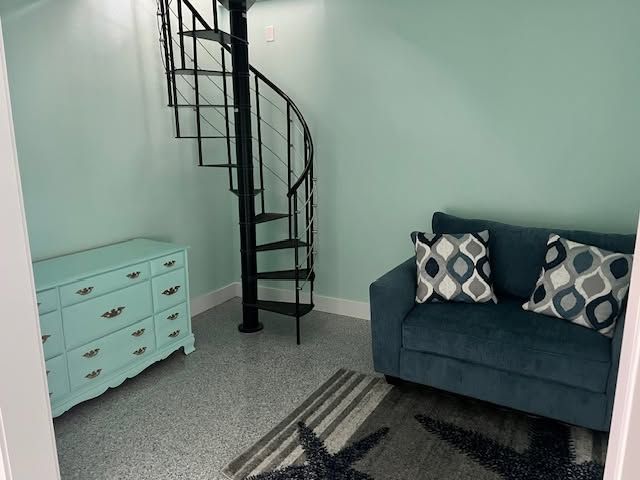 Small room with a spiral staircase, teal dresser, blue sofa, and patterned rug on gray carpet.