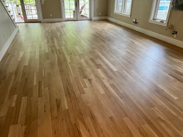 Empty room with light wood floors, beige walls, and large windows and French doors.