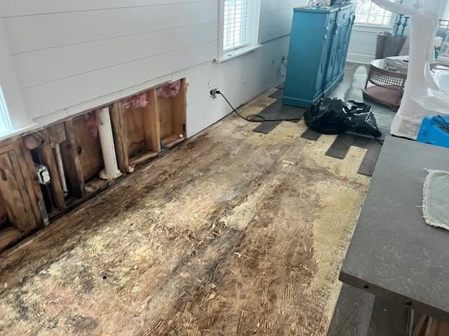 Damaged room with removed flooring, exposed wall studs, and construction materials near a window.