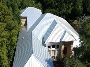 Aerial view of a white metal-roofed house surrounded by dense green trees