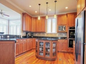 Warm wood kitchen with black countertops, central island, stainless appliances, and pendant lights