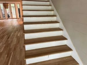 Staircase with white risers and wood treads in a bright hallway with hardwood floors.