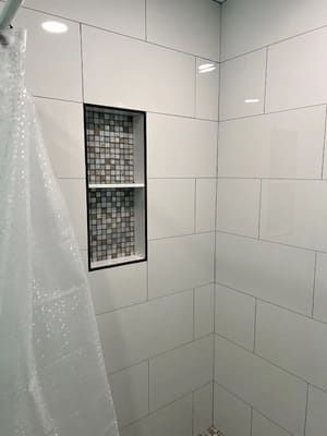 White tiled shower with a recessed mosaic shelf and a translucent shower curtain on the left.