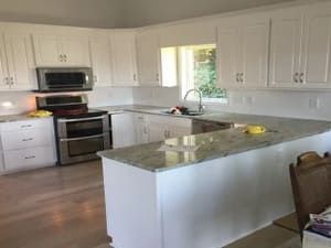 Bright white kitchen with stainless steel appliances, granite island, and wood floors