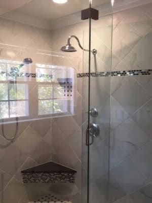 Glass shower with tiled walls, chrome showerhead, corner shelf, and window reflection
