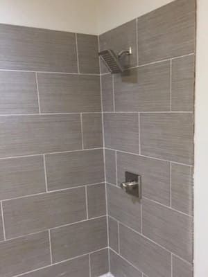 Corner shower with gray tile, chrome showerhead, and wall-mounted faucet or control.