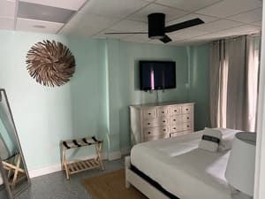 Coastal-style bedroom with white bed, dresser, wall-mounted TV, curtains, and mint green walls