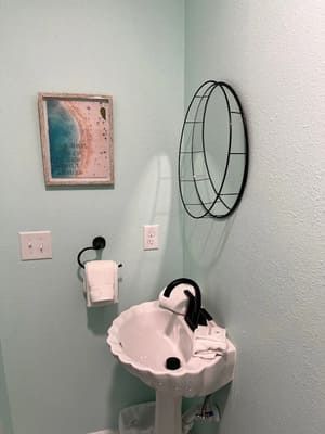 Small mint bathroom with a white pedestal sink, towel ring, wall art, and black wire mirror.