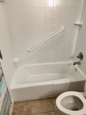 Accessible bathroom with bathtub, grab bar, wall fixtures, and toilet seat in foreground