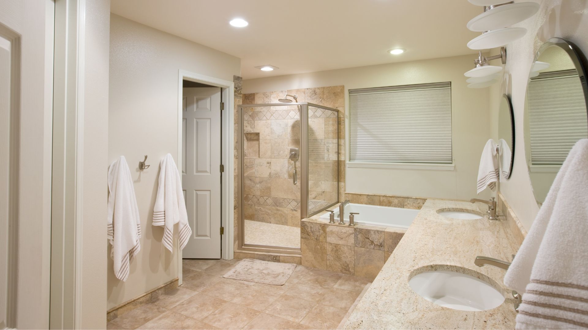Spacious beige bathroom with double vanity, walk-in shower, soaking tub, and towels hanging on the wall