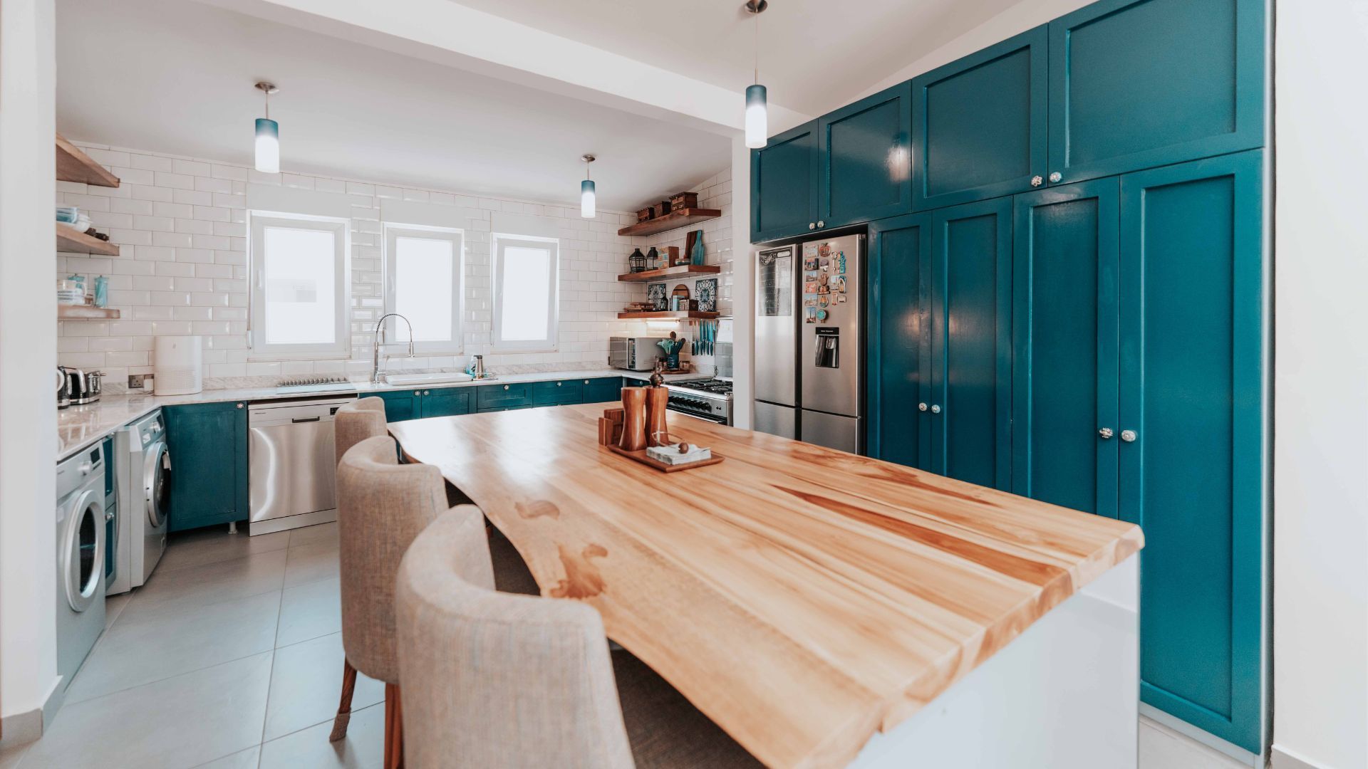Bright modern kitchen with teal cabinets, wooden island, and bar stools near windows