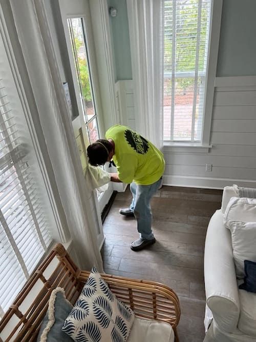 Person cleaning a windowsill in a bright living room with white curtains and a sofa