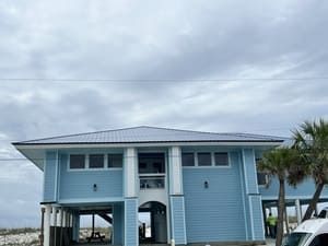 Blue stilt house with a metal roof on a beach under cloudy skies