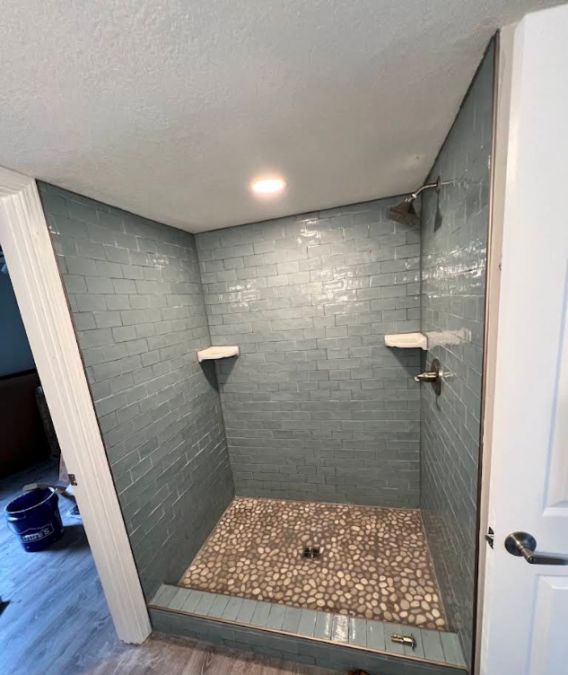 Empty tiled walk-in shower with gray walls, pebble floor, and built-in corner shelves