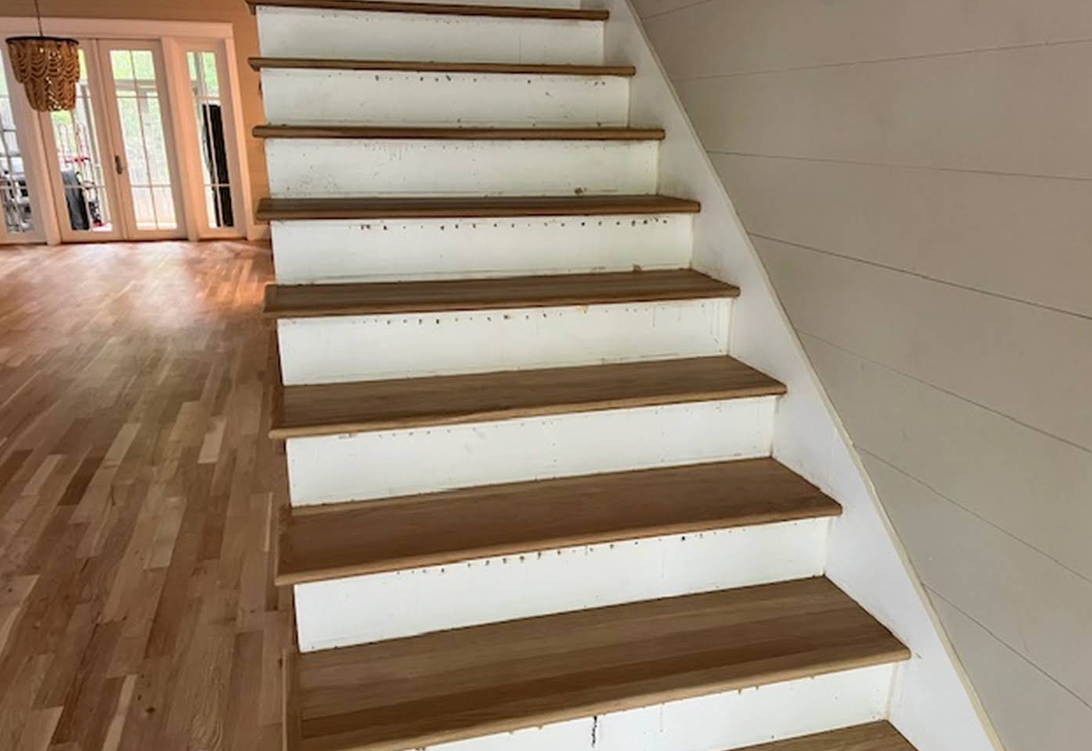 Wooden staircase in a bright, empty hallway with hardwood floors and white walls