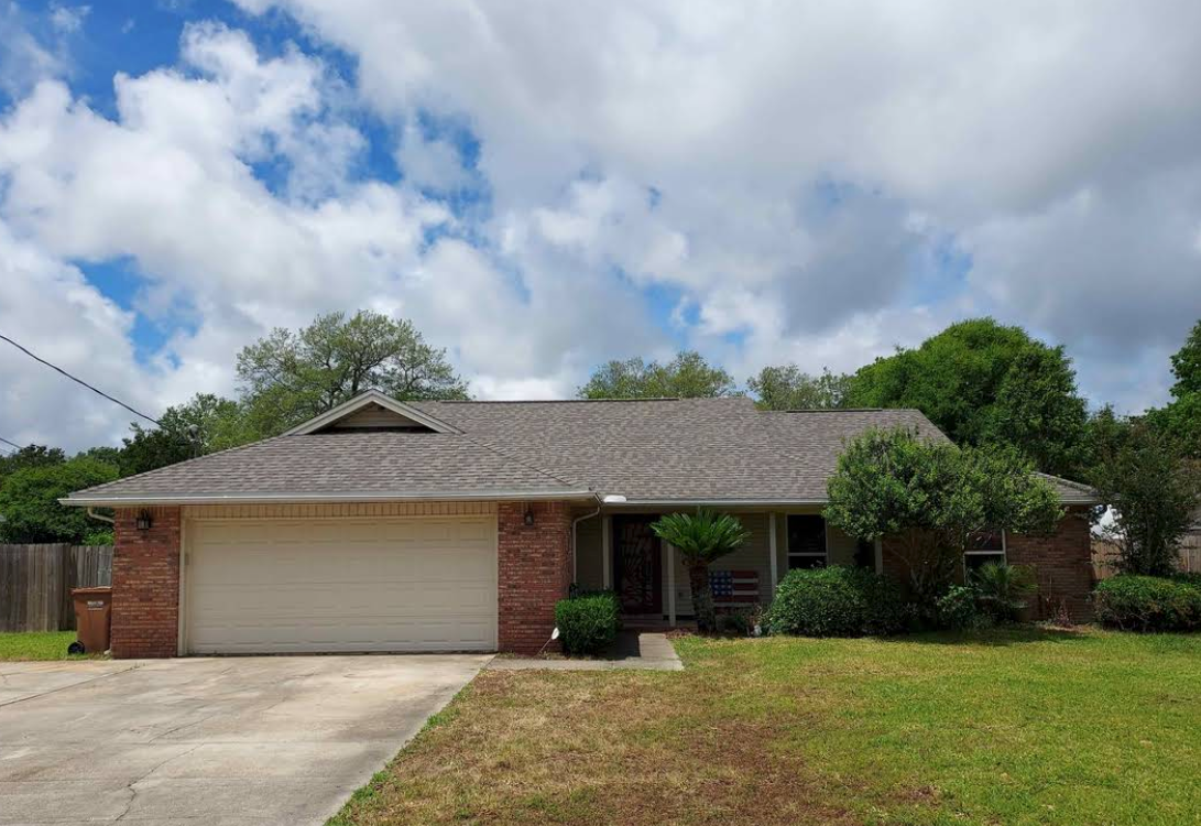 Single-story brick house with two-car garage, front lawn, and cloudy sky