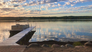 A boat is docked at a dock on a lake at sunset.