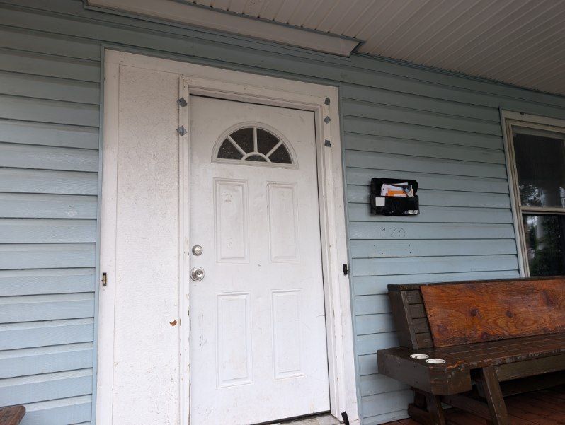 White front door on a light blue house porch with a wooden bench and mailbox nearby