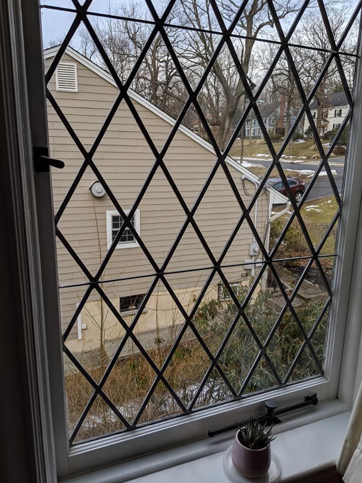 A window with a wrought iron grid on it is looking out to a house.