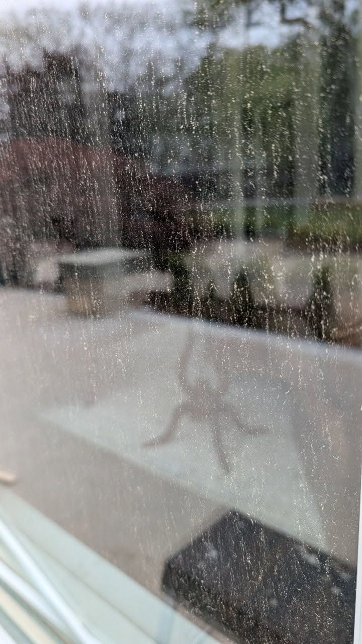 Rain-speckled window overlooking a patio with outdoor tables and chairs reflected in glass