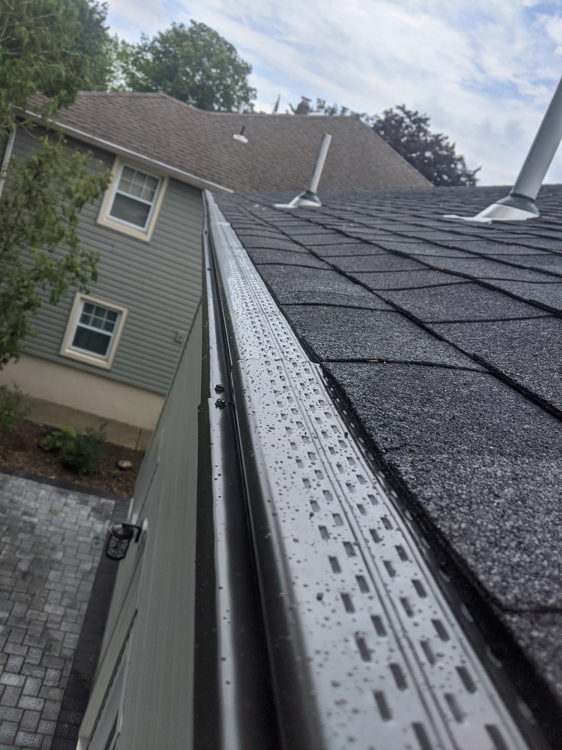 A gutter on the side of a house with a roof in the background.