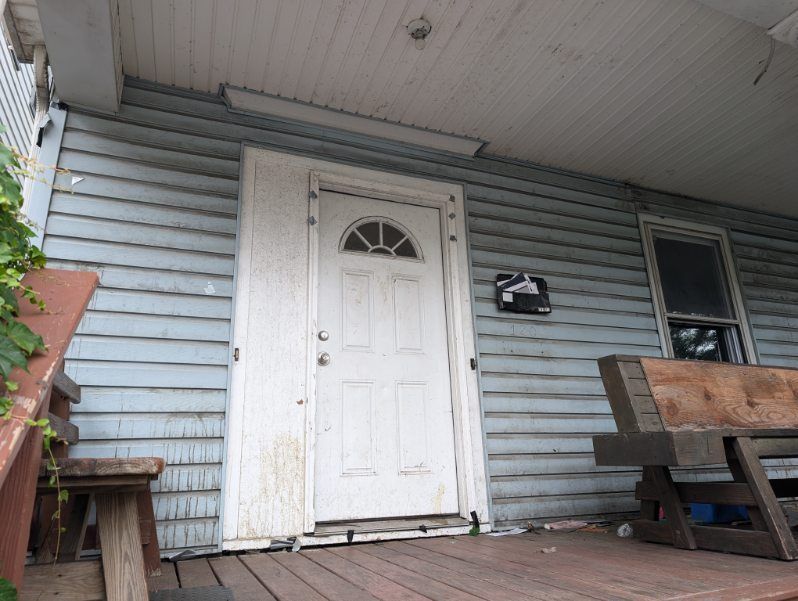 Front porch with white door, blue siding, and a bench under a covered ceiling