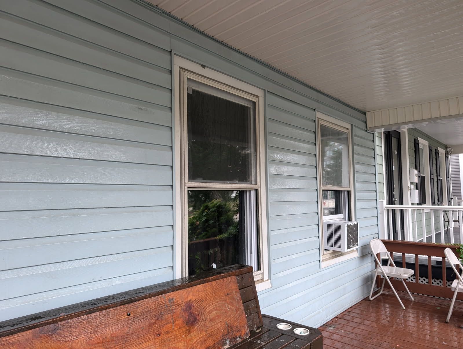 Covered porch with light blue siding, windows, and a wooden bench along the wall