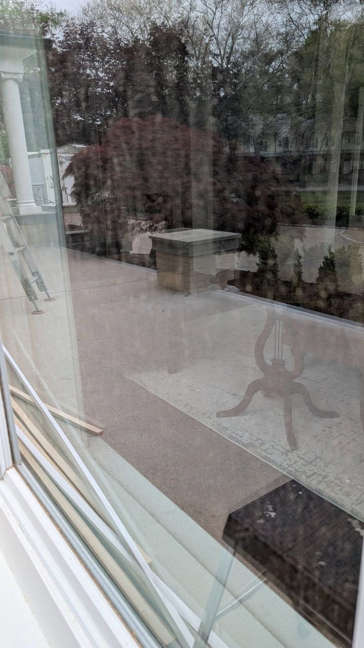 Rain-streaked glass window reflecting a patio with outdoor furniture and plants.