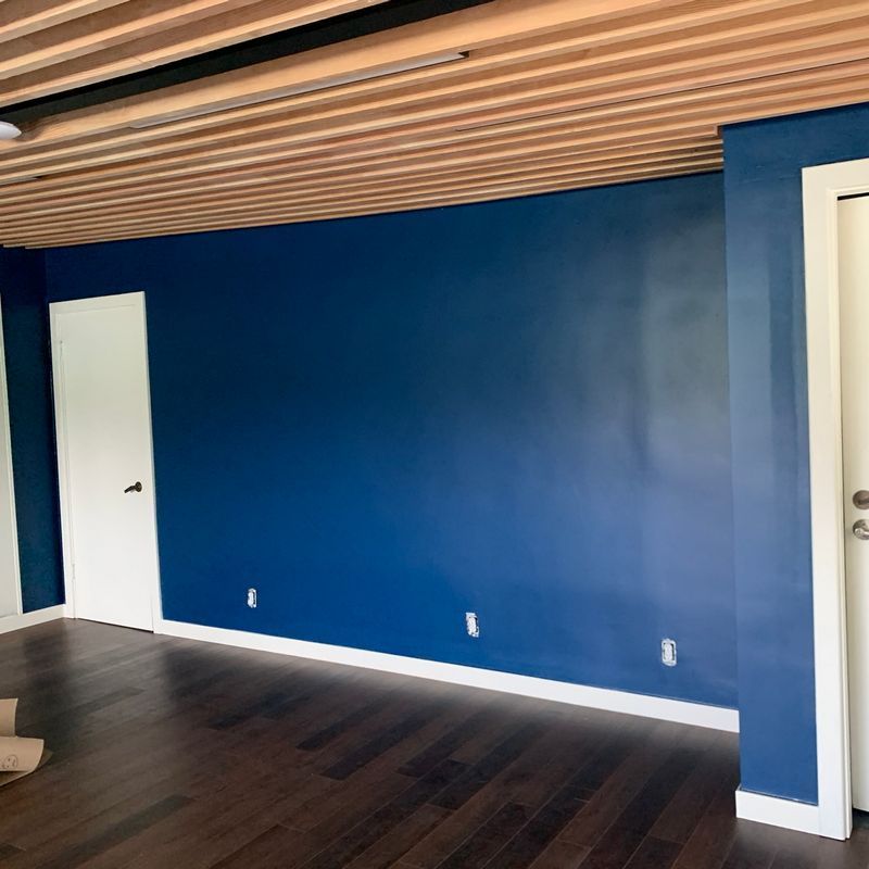 Empty room with blue accent wall, white door, dark wood floor, and slatted wood ceiling