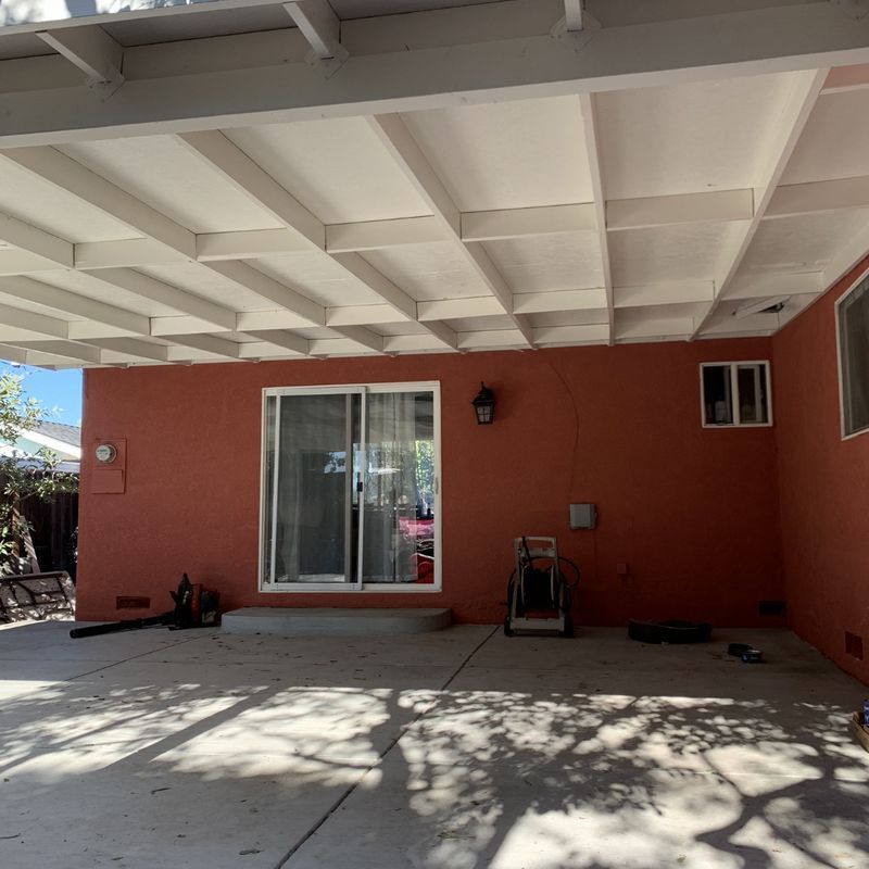 Covered patio with orange wall, sliding glass door, and concrete floor in daylight.
