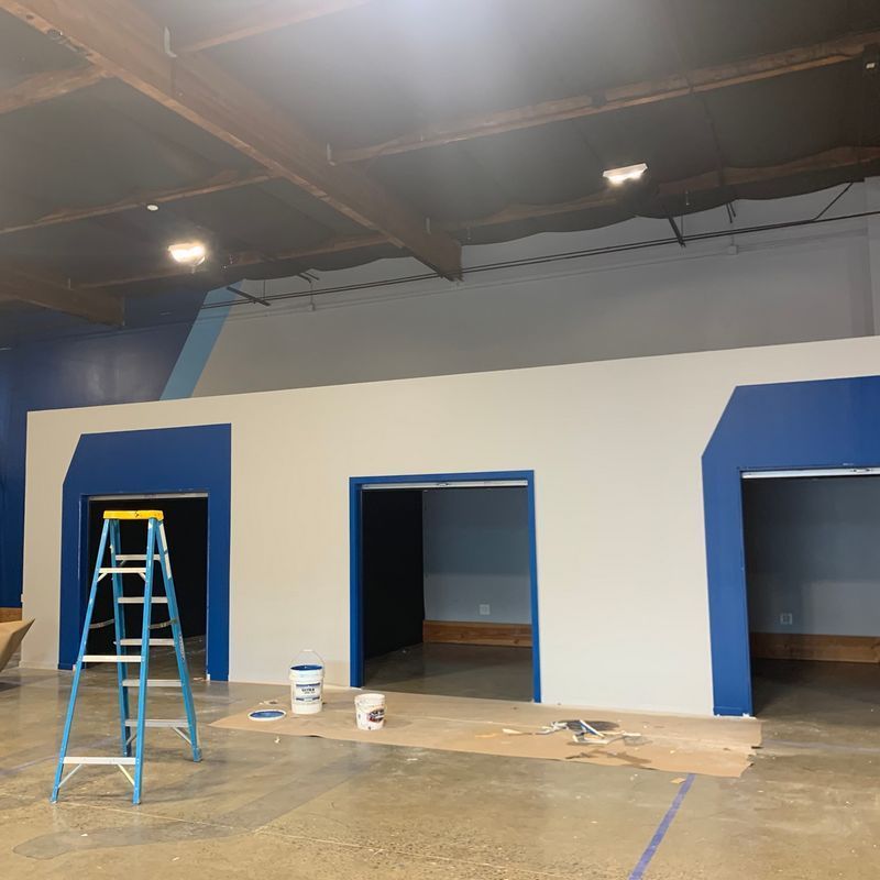 Three open doorways in a blue-and-white interior under construction, with a ladder and paint supplies on the floor