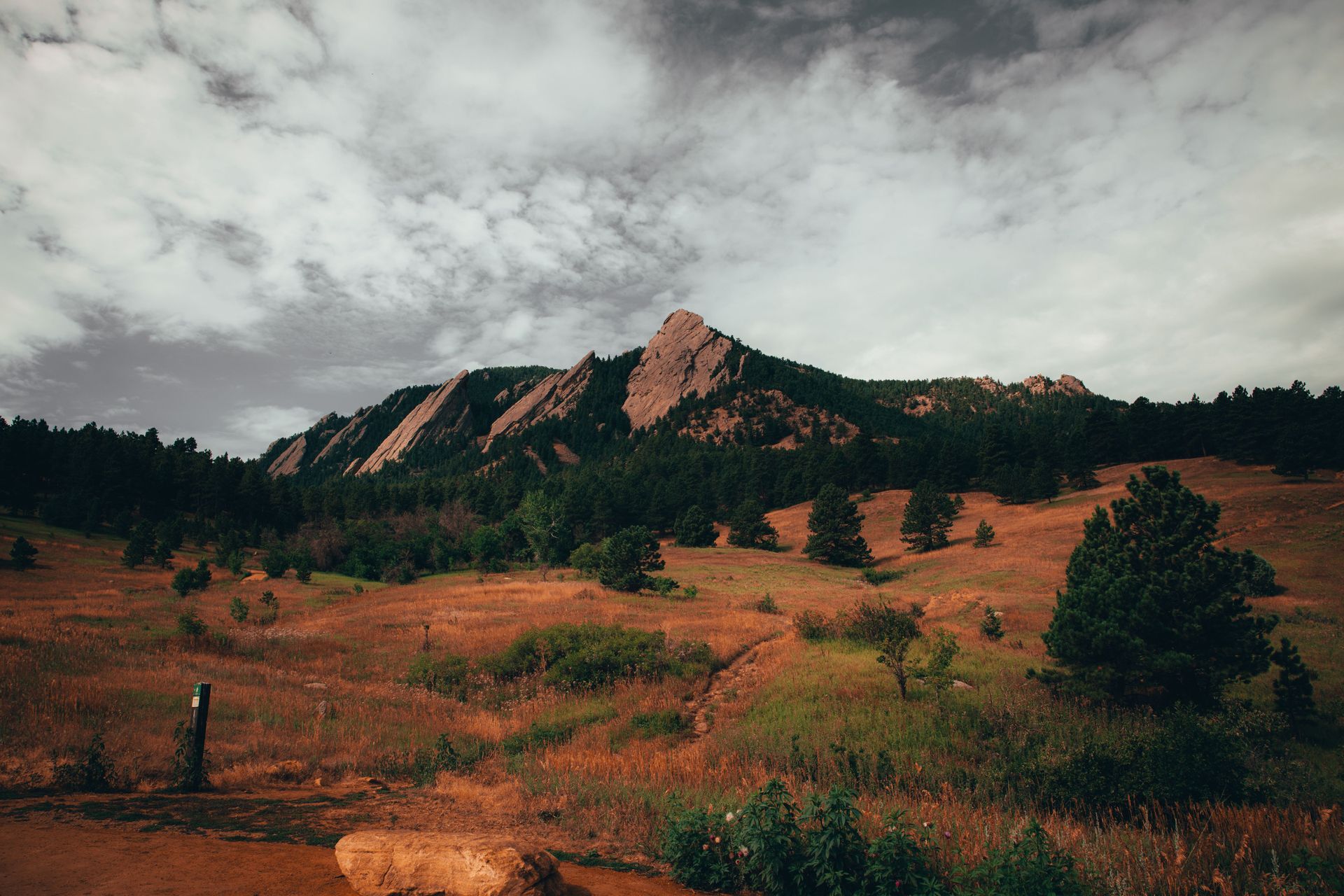 Rocky mountain ridge above orange grassland under a cloudy sky