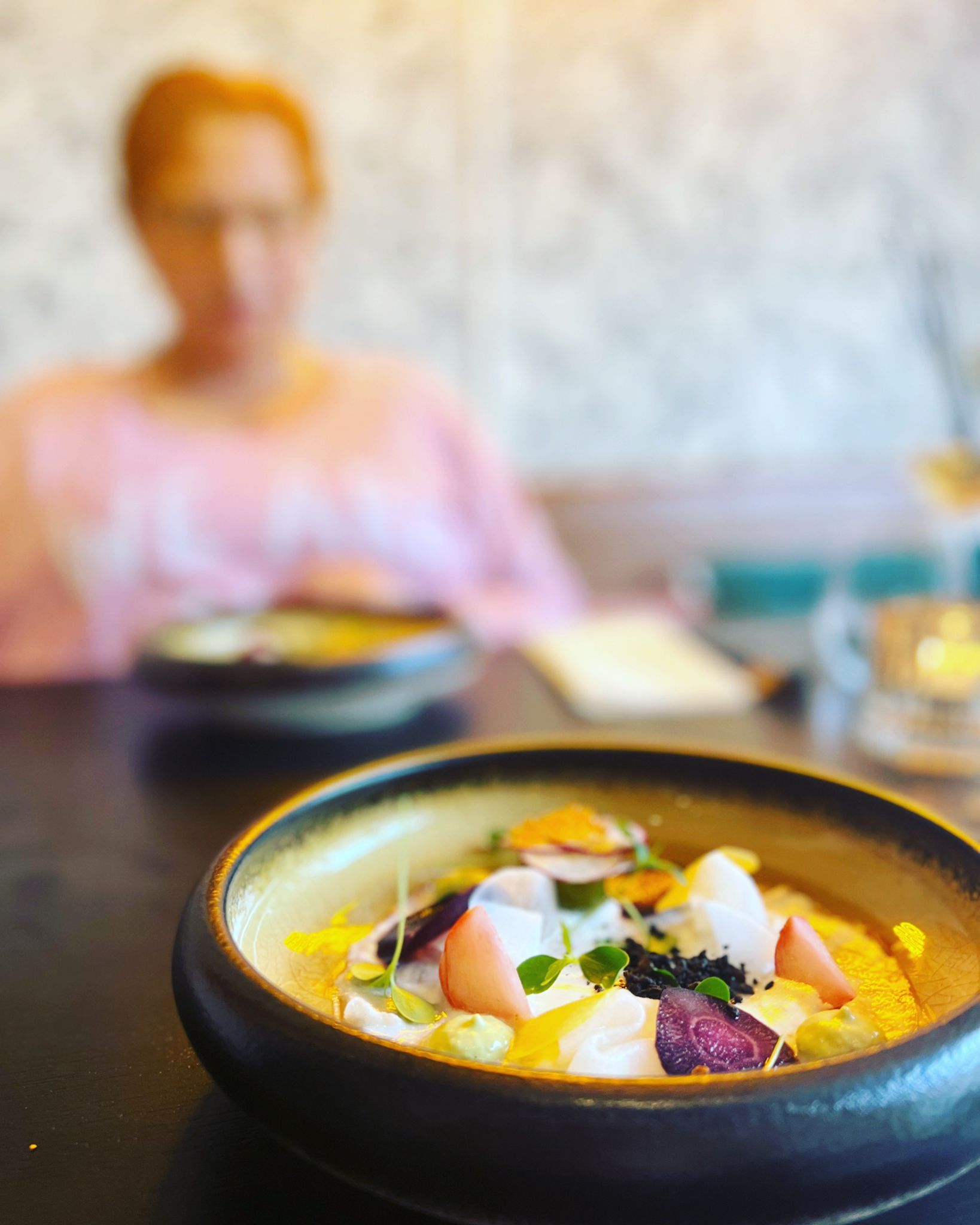 Een fine-dining gerecht op de voorgrond op een tafel, met een wazig persoon erachter.