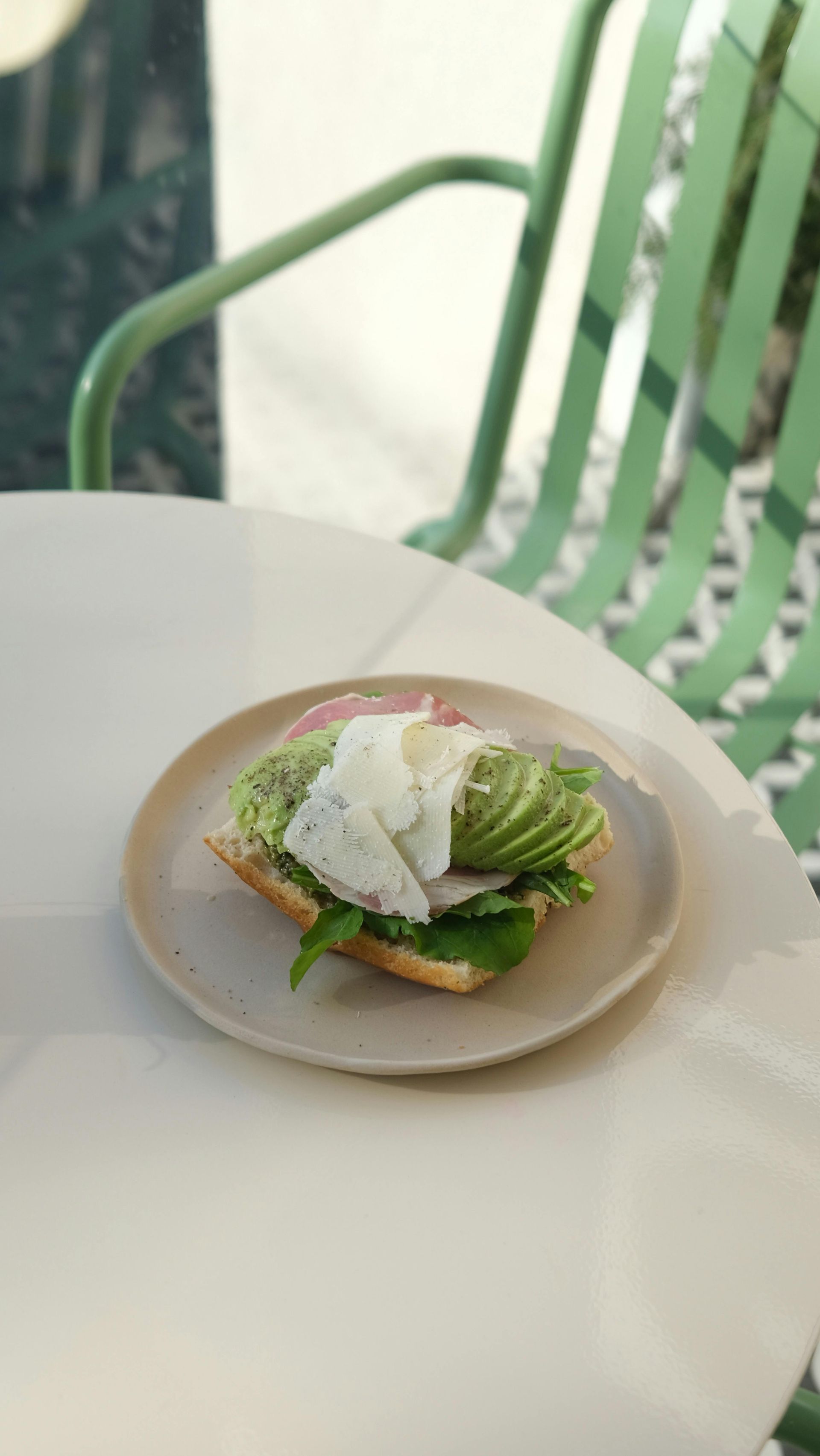 Een klein bordje met toast, avocado en een gepocheerd ei op een witte tafel, met een groene stoel op de achtergrond.
