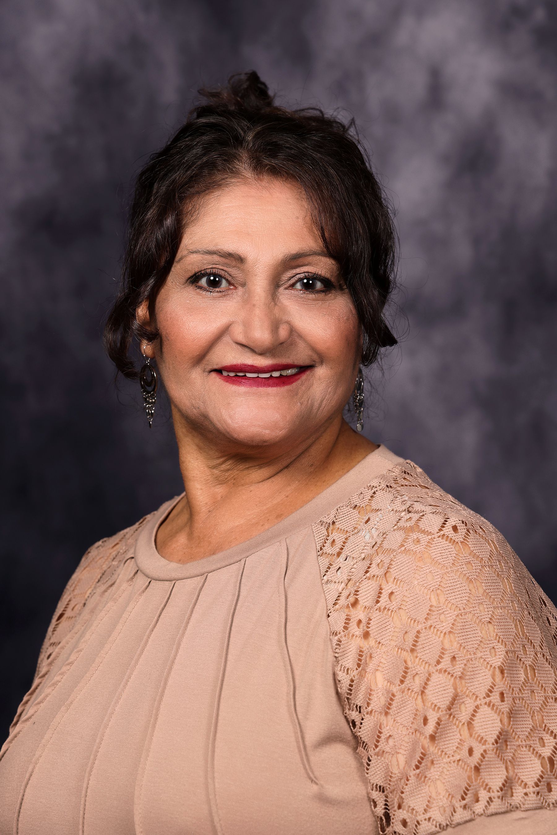 Woman wearing glasses smiling, wearing a pink shirt, in front of a dark blue background.