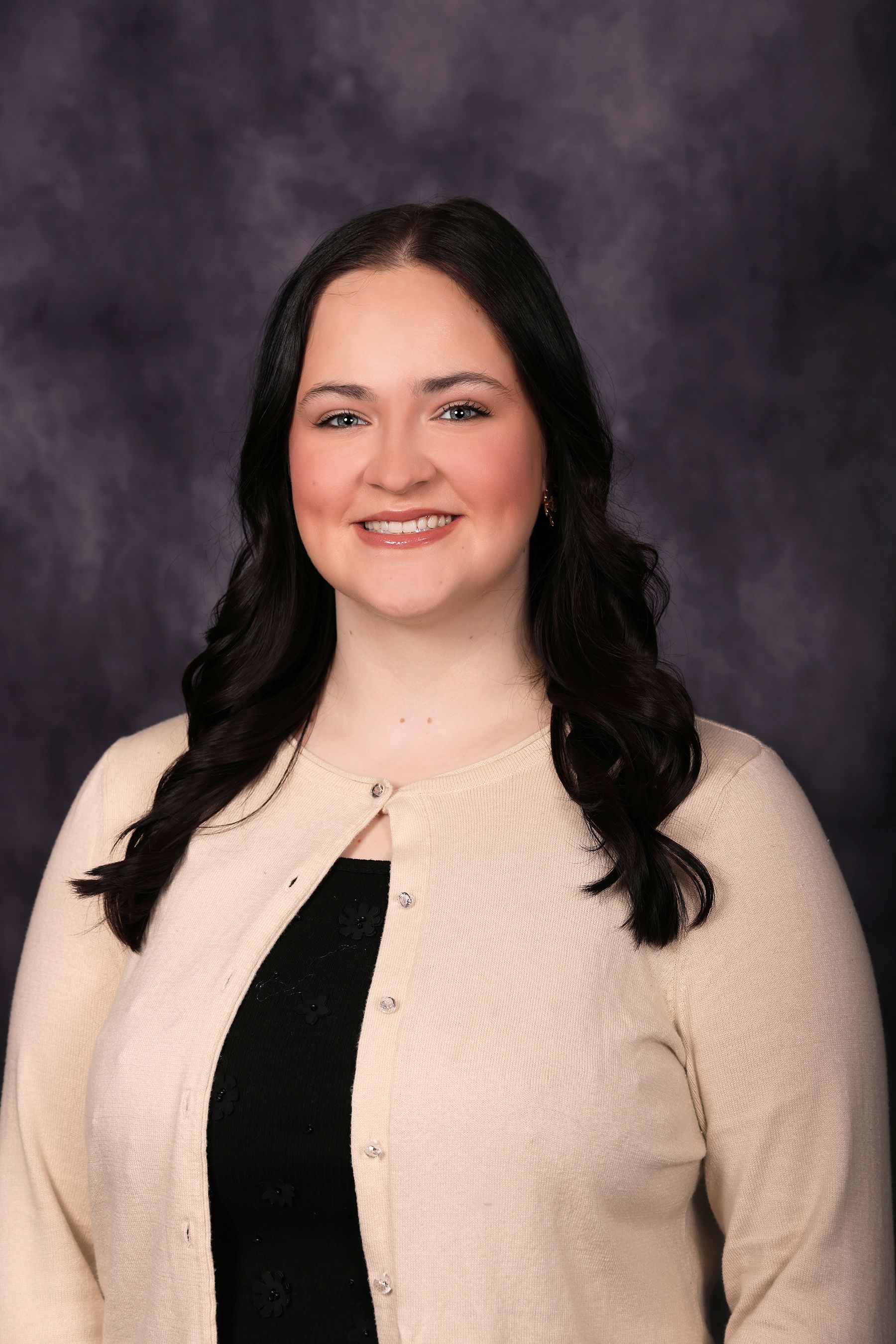 Woman with curly light brown hair smiles, wearing a gray blazer over a lavender top.