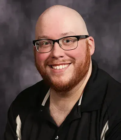 Bald man with glasses and red beard smiles at the camera, wearing a black shirt.