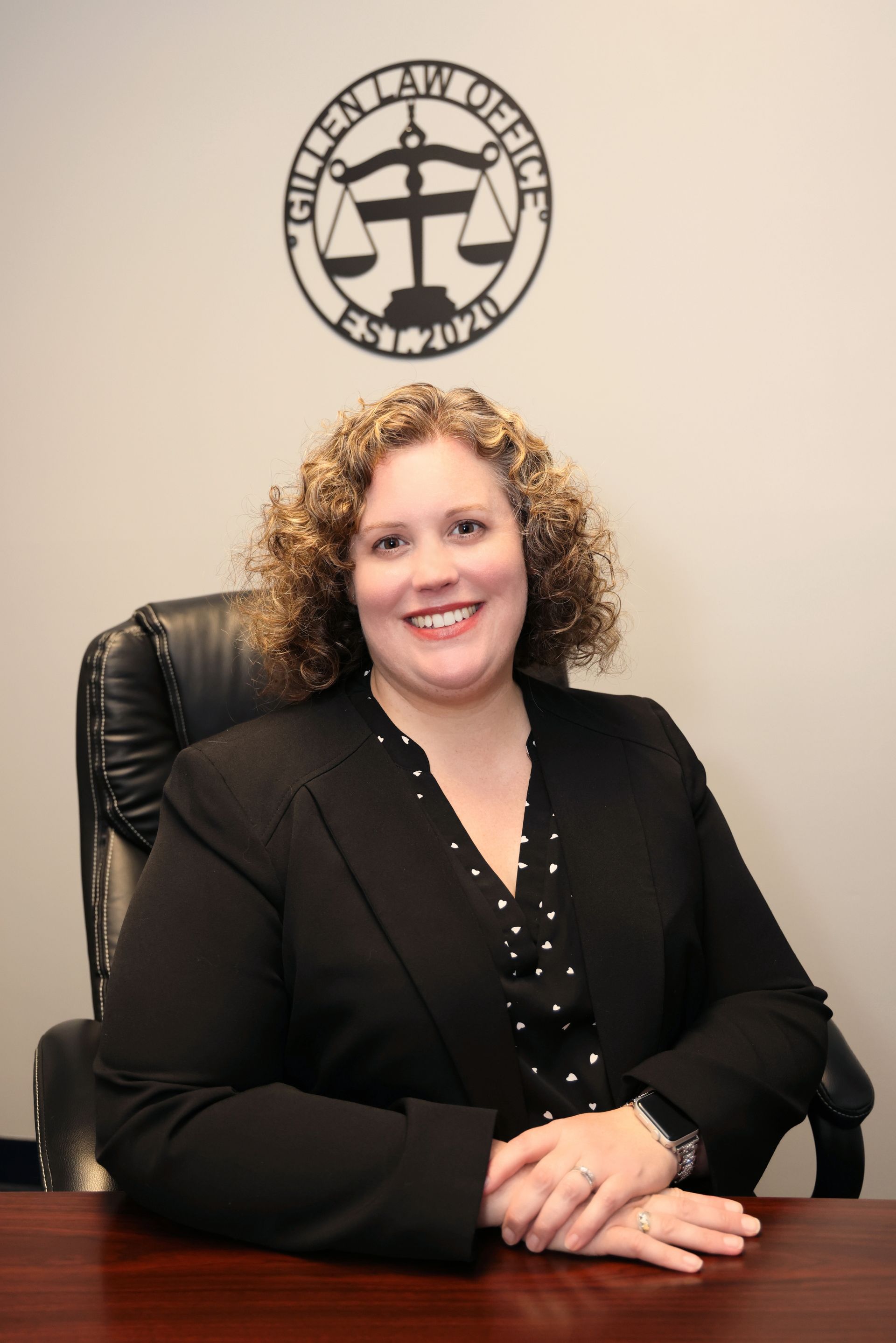 Woman with curly light brown hair smiles, wearing a gray blazer over a lavender top.