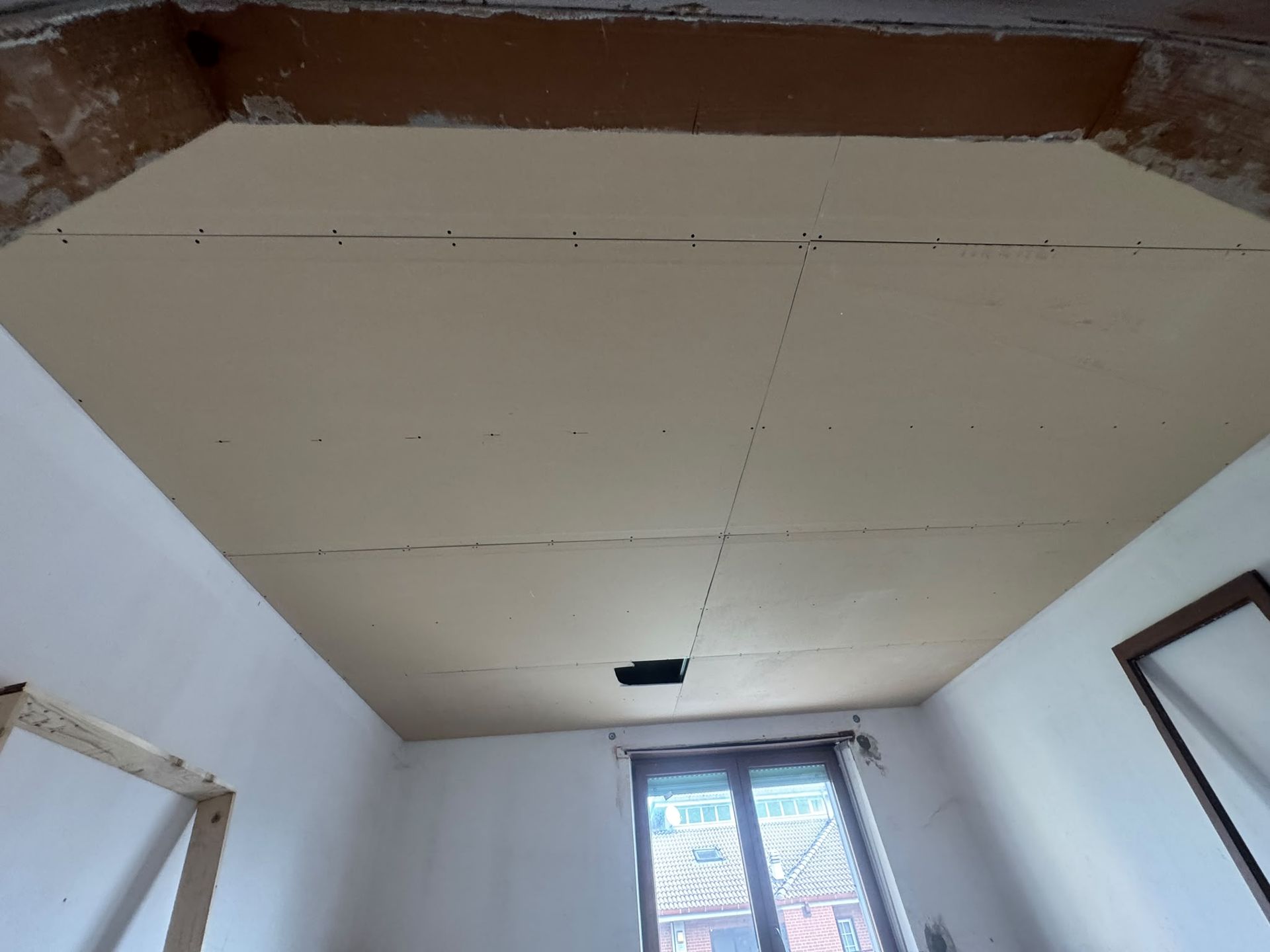 Stanza non finita con soffitto beige, pareti bianche e una finestra in fondo.
