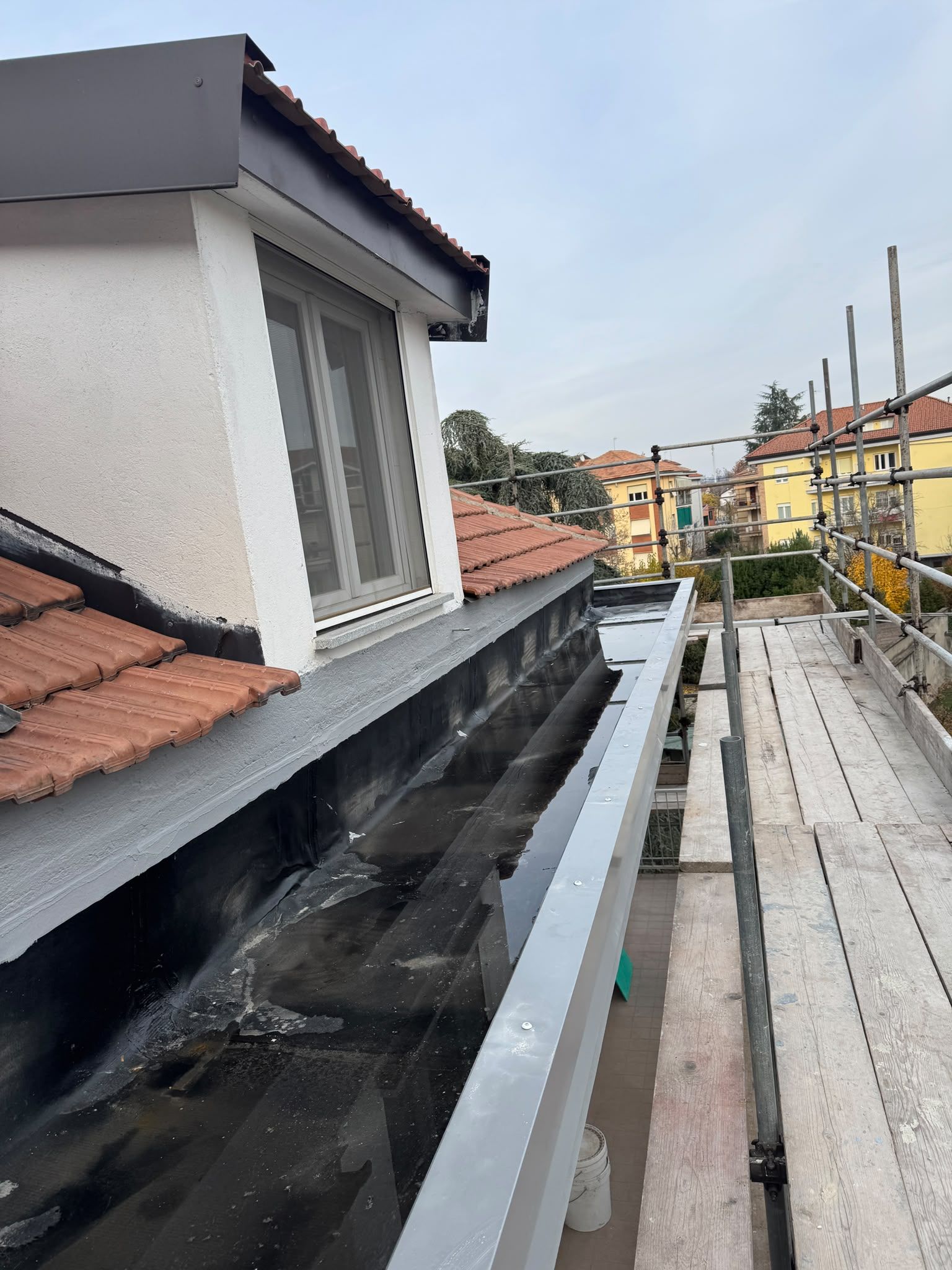 Lavori di copertura su una casa con tegole rosse, impalcatura e grondaia parzialmente installata lungo il bordo del tetto