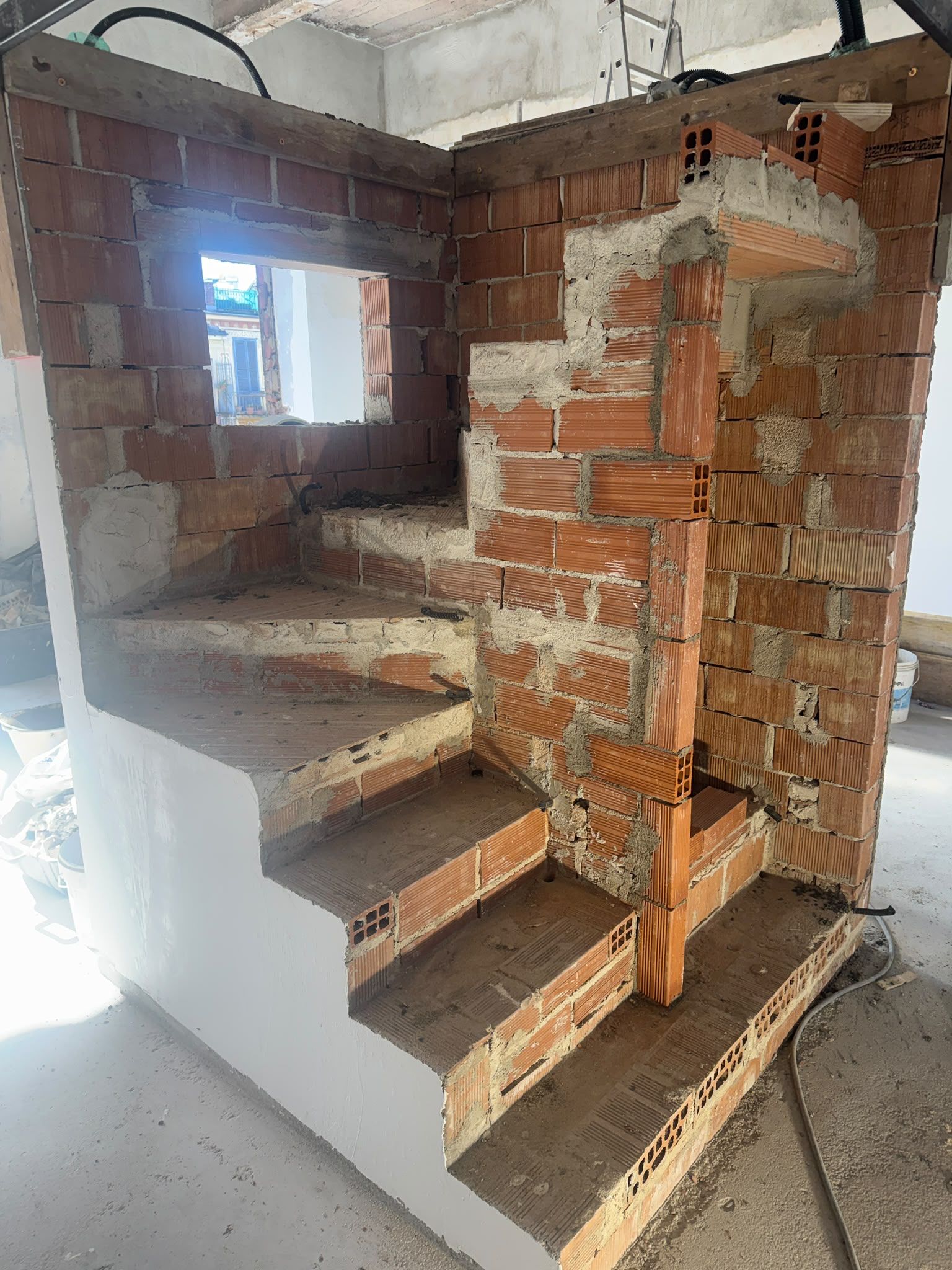 Vano scale interno in costruzione, con mattoni a vista, gradini in cemento e pareti non finite.