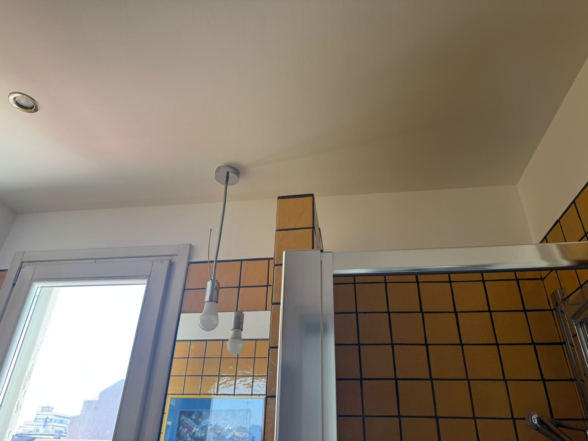 Bagno con parete della doccia piastrellata di arancione e soffitto bianco, visto da vicino a una finestra.