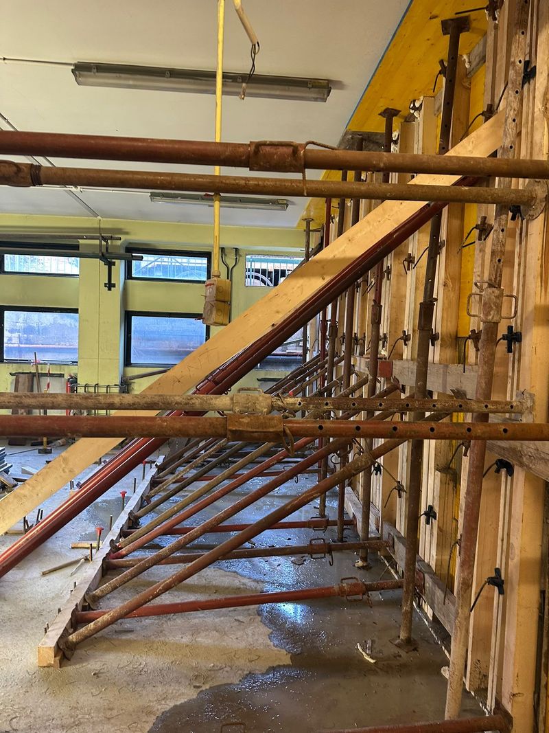 Interno di un cantiere con puntelli di legno per le impalcature e pavimento in cemento fresco accanto alle finestre