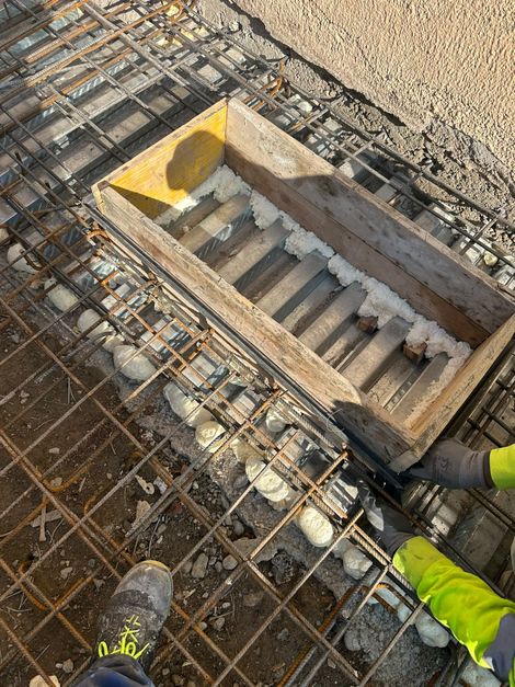 Apertura nel solaio in cemento armato di un cantiere, con stivali da lavoro e indumenti ad alta visibilità visibili ai bordi